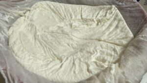 Homemade Greek yogurt straining through cheesecloth in a mesh strainer.