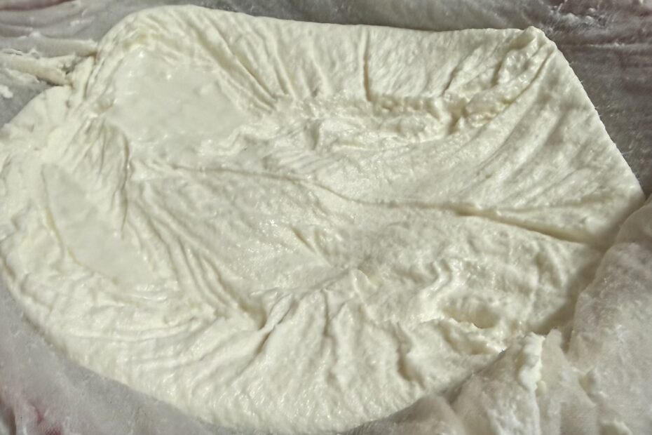 Homemade Greek yogurt straining through cheesecloth in a mesh strainer.