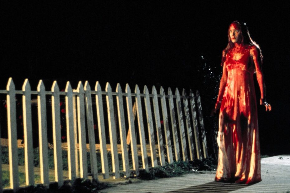 Carrie White drenched in blood, walking home at night beside a picket fence in Carrie (1976).